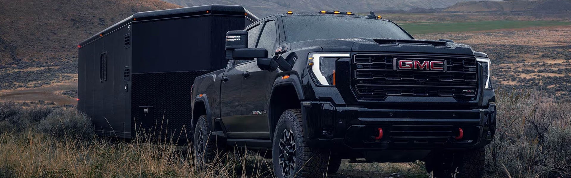 A black GMC Sierra 2500 towing a trailer through a field.