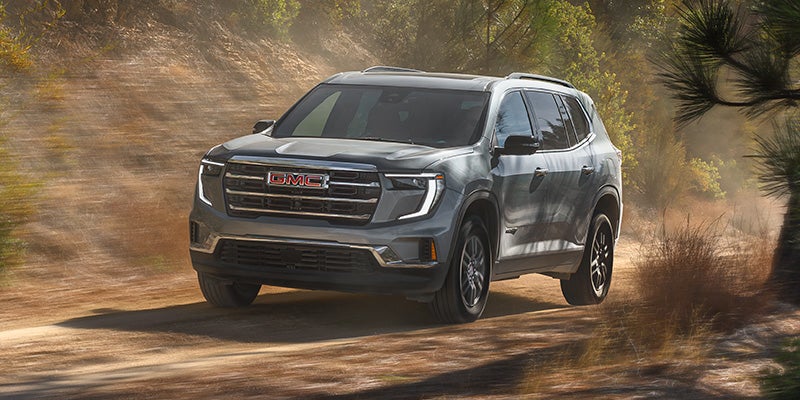 2027 GMC Acadia Elevation in Sterling Metallic driving on a forest road