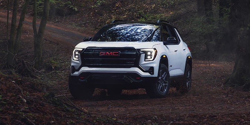 2027 GMC Terrain AT4 in Summit White with Ebony Twilight Metallic roof driving on a forest trail